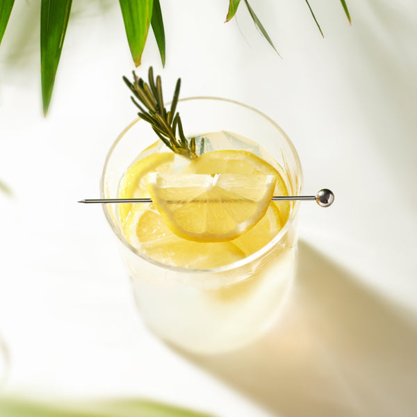 Pique à cocktail Final Touch posée sur un verre garni de citron et de romarin.